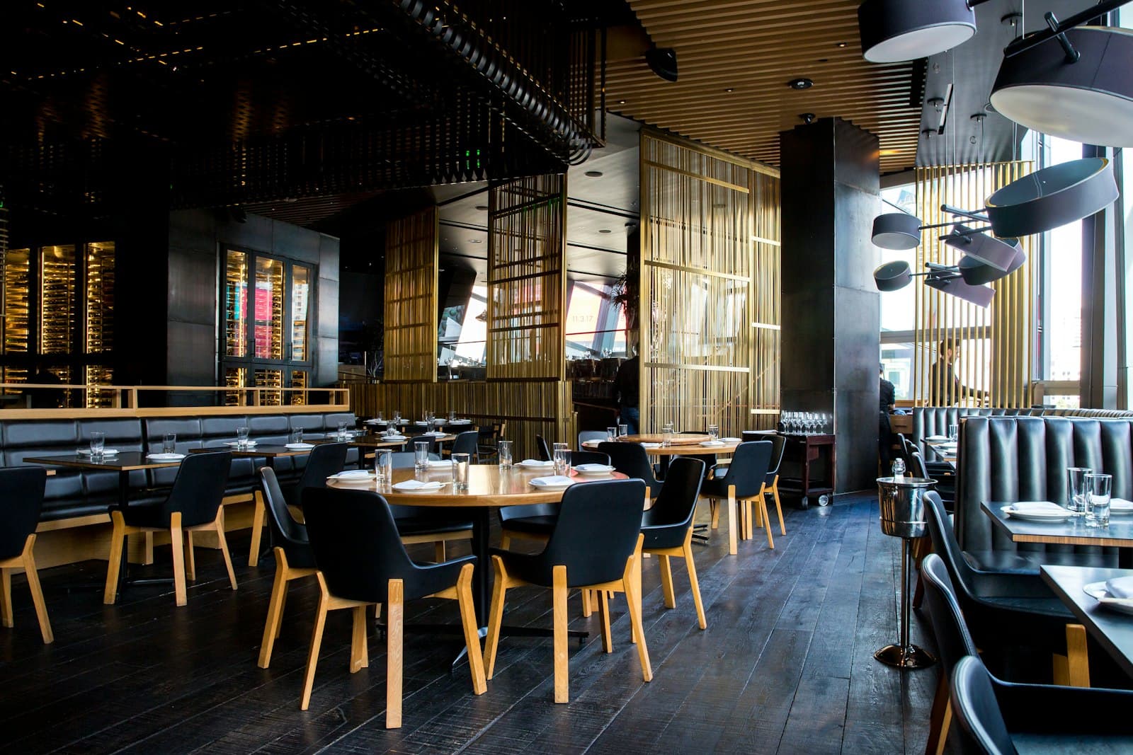 A dining room with timber tables, black chairs, and brass screen dividers.